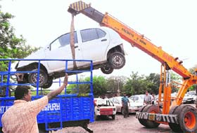 A crane of the Municipal Corporation puts an impounded car on a truck at the Motor Market in Sector 48 on Wednesday