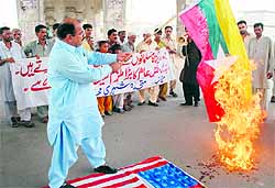 A Pakistan protester stands over a US flag as he holds up a burning Myanmar flag during a protest in Multan