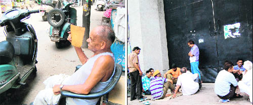 An elderly man sitting outside his office fans himself to beat the heat; and (right) with work remaining suspended due to power failure, workers play cards outside a factory in Amritsar on Monday.