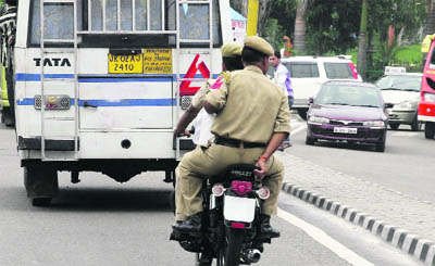 Two policemen ride a motorcycle without registeration number plate and helmets at Secretariat road in Jammu on Friday. 