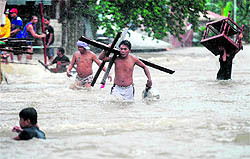 Residents carry their belongings as they wade through flood waters after a river overflowed following torrential rain in Manila on Tuesday