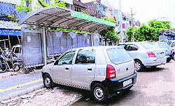 Cars haphazardly parked in front of a modern bus queue shelter