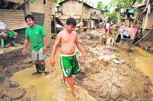 Residents walk through the mud left by the floods at a slum next to a river in San Mateo town near Manila on Sunday