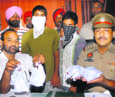 Inspector Kewal Krishan, CIA in charge, shows the heroin recovered from two drug peddlers (face covered) in Jalandhar on Friday. 