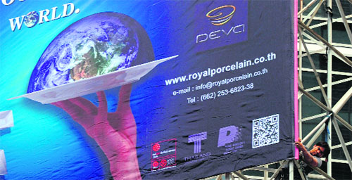 A worker puts an advertising banner on a building in Bangkok on Monday. Thailand's Office of the National Economic & Social Development Board (NESDB) lowered this year's GDP target from 5.5-6.5 to 5.5-6 per cent due to the impact of the eurozone debt crisis and the US economic slowdown.