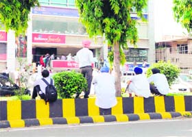 Visitors rest on a divider in front of Passport Kendra on the busy Mall Road, in Amritsar