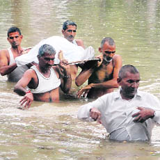  Family members carry a body in waist-deep water from the Civil Hospital in Gohana on Monday. 