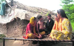 A West Pakistan refugee family sitting on a charpoy outside their kutcha house