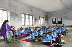 Students sit on the floor in a classroom with damp walls