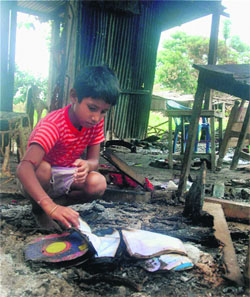 A boy looks at his burnt textbooks at his gutted house that was torched by rioters during ethnic violence at Kharabari Charak Pally in Barpeta district of Assam.