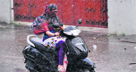 A girl drives through a road on a two-wheeler during rain in Ludhiana.