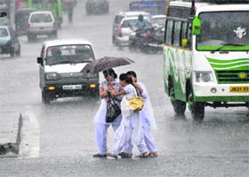 Girls huddle under an umbrella to cross a road during heavy rain in Jammu on Thursday