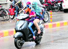 Two girls ride a scooter in the rain in Amritsar on Saturday.