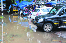 Vehicles parked in front of a puddle in the Lal Chowk area after rain lashed Srinagar on Sunday. Motorists had tough time negotiating potholes. 