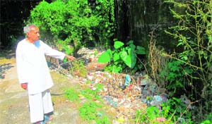 An old-aged person points to the choked drain with waste and filth passing through the private premises of five senior citizens in Kangra town.