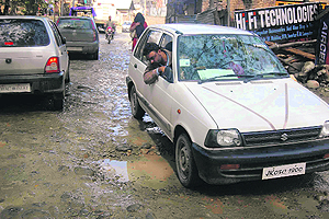 A commuter tries to dodge a pothole in vain on the road leading to Bijbehara railway station in Anantnag.