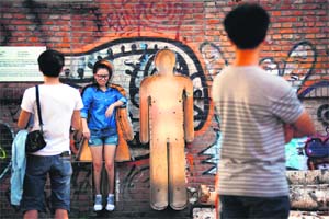 Bystanders watch a woman as she steps out of a human-shaped cavity in a wall at an art district in Beijing