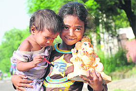 A girl holding a baby tries to sell an idol of Lord Ganesha in Jammu on Sunday.