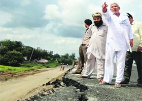 People look at cracks in a newly built road near Shamgarh in Karnal