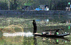A fisherman throws his net in the Dal Lake as policemen stand guard on the banks of the lake in Srinagar on Thursday