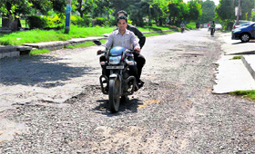 Motorists ride on a damaged road in Sector 13, Karnal.