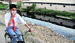 A student covers his nose while cycling along the Budha Nullah near Kundan Puri in Ludhiana