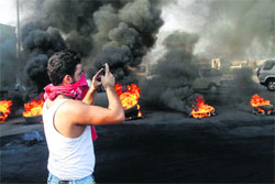 A masked man photographs burning tyres used as a roadblock to protest the death of head of the intelligence division of domestic security forces, in Sidon.  AP/PTI