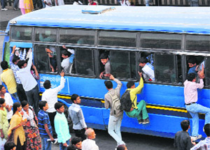 Students hanging on to the doors and windows of a bus.
