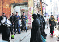 Security personnel stand guard as women walk to buy essential items during relaxed hours of curfew in violence-hit Faizabad on Monday.  PTI