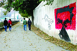 People walk past a graffiti written on a wall of the Jhelum bundh in Srinagar on Monday.