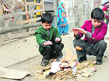 Two schoolchildren try to keep themselves warm by buring waste papers and dry grass in Srinagar on Saturday