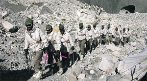 Army personnel trek a rugged mountain range.