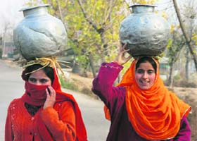 Women carry water in metal pitchers on their heads on Srinagar-Baramulla highway