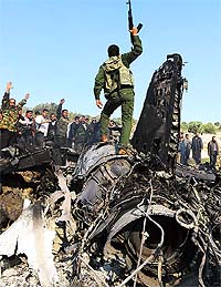 Rebels celebrate on top of the remains of a government fighter jet which was shot down at Daret Ezza on Wednesday