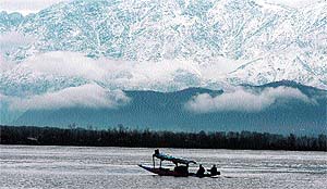 A boat passes in front of snow-covered mountains on the Dal Lake in Srinagar on Thursday