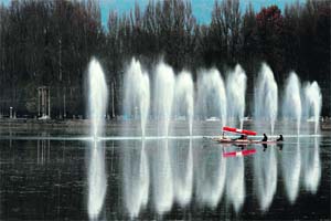 Shikara boatmen transport tourists past water fountains on Dal Lake