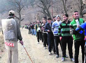 A police personnel stands guard as youths wait in a long queue during a recruitment drive by the J&K Forest Department in Anantnag on Sunday.
