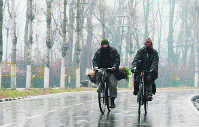Two men ride their bicycles in the rain in Srinagar on Thursday. The cold wave further tightened its grip in Jammu and Kashmir with most places in the state recording sub-zero temperatures. 