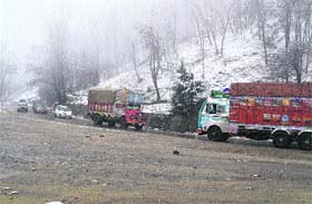 Trucks pass through Qazigund on the Srinagar-Jammu National Highway after the area witnessed a moderate snowfall on Thursday
