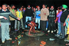 People gather around an open manhole in Parasram Nagar wherein a child was believed to have fallen on Friday evening. A worker of the Sahara Jan Sewa makes a futile attempt to locate the kid as the news turned out to be a hoax.