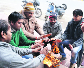 People sit by a bonfire to keep themselves warm on a chilly day. A resident makes way through heavy fog in Amritsar on Sunday.