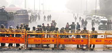 Riot police keeps watch along a barricaded road leading towards India Gate following clashes in New Delhi on Monday
