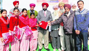 Dr Baldev Singh, deputy director, state education department, distributes uniforms among schoolchildren at Government Senior Secondary School, Akhara.