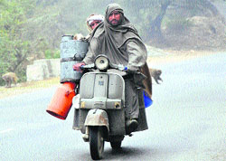 A man wrapped in a shawl rides a scooter on a cold, foggy morning on the outskirts 