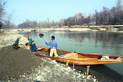 Workers unload sand from a boat after collecting it from the surface of the river Sindh in Ganderbal on Sunday. 