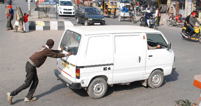A man pushes a van which broke down at a crossing on a busy road in Bathinda. 