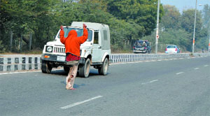 A beggar courts danger by refusing to leave the road while vehicles travelling at high speed zoom past.