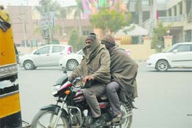 Combating cold: Two men wrap themselves in woollens while riding a motorbike in Bathinda