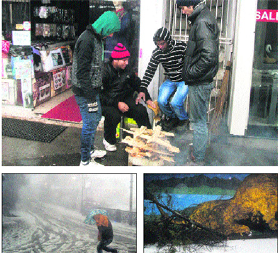 Shopkeepers warm themselves by lighting a fire in Mussoorie. A tree uprooted on Mall Road due to the strong winds. A tourist runs for cover due to snow and strong winds in Mussoorie on Friday.