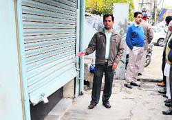 A man shows the broken shutter of an office in Ghumar Mandi. 